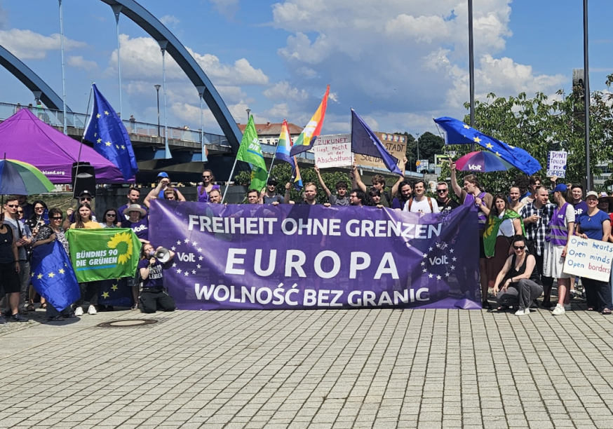 grupa protestujących, tłum gromadzi się wokół baneru w dwóch językach - polskim i niemieckim, o treści