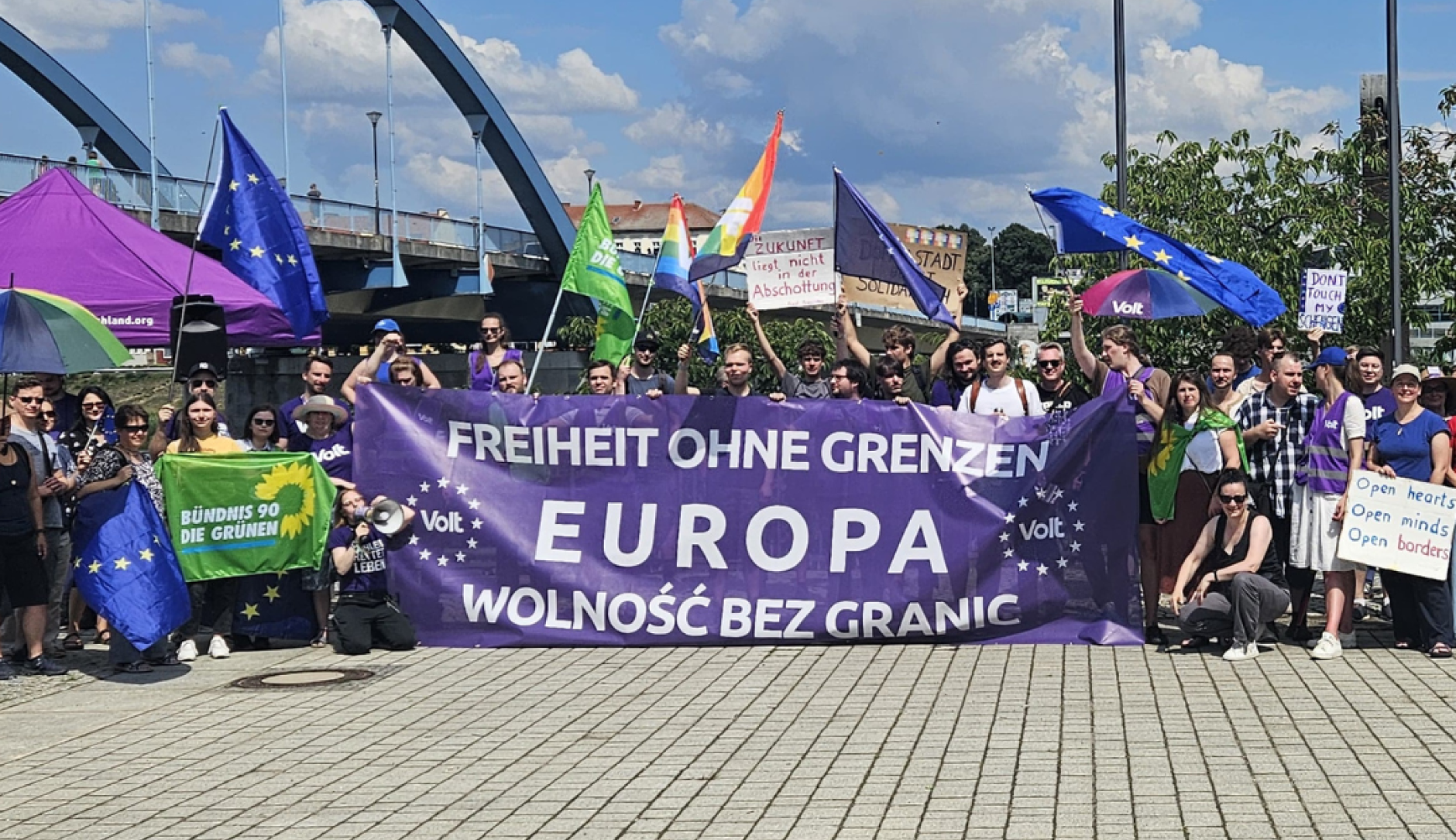 grupa protestujących, tłum gromadzi się wokół baneru w dwóch językach - polskim i niemieckim, o treści