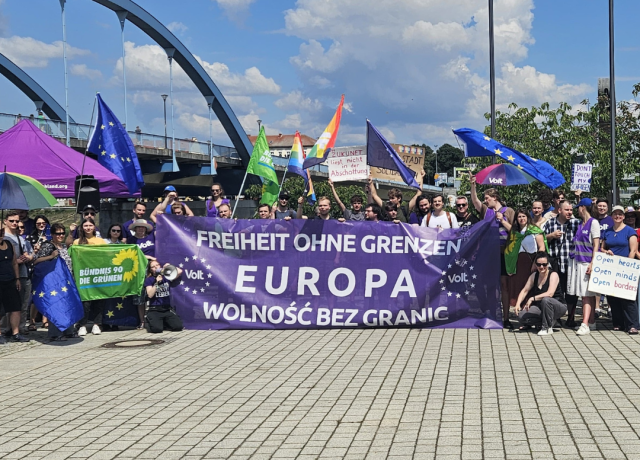 grupa protestujących, tłum gromadzi się wokół baneru w dwóch językach - polskim i niemieckim, o treści 