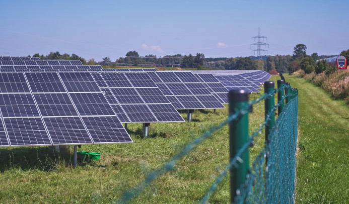 rzędy paneli słonecznych z infrastrukturą energetyczną w tle i pociągiem